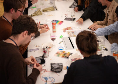 Photo of a table covered in beads and crafting supplies, with Celebration of Design attendees assembling bracelets around it.