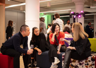 Photo of a group of four Celebration of Design attendees sitting and enjoying a conversation, with a crowd in the background
